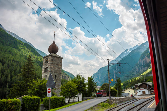 View of Pfarrkirche St.Niklaus with forest and mountains on background from panoramic train. Station St.Niklaus in canton of Valais