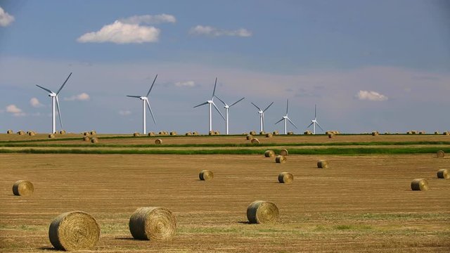 Renewable energy wind turbines in a harvested agricultural field with bales hay in the Canadian prairies of Alberta, Canada.