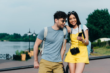 handsome man and asian woman smiling and looking at smartphone