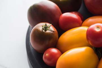 close up view of red and yellow tomatoes on wooden pizza pan on marble surface