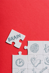 top view of unfinished white puzzles near separate piece with brain lettering isolated on red