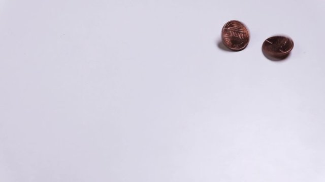 Two different coins of one cent denomination rotate and stop in the frame. Copy space. US Small Metal Cash. Movement on a white table. The concept of poverty and wealth.