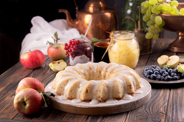 Obraz na płótnie Canvas Iced sugar cake with apples on tray, cooper teapot, jars of sorbet