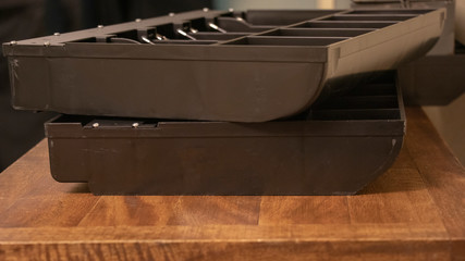 A close up shot of two black and metal cash drawers stacked crookedly on top of each other resting on a light wooden table.