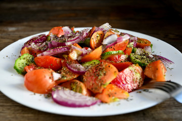 Summer salad of tomatoes, cucumbers, spices and herbs in a white plate on a wooden table.