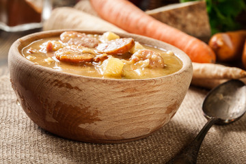 Wooden bowl of split pea soup with sausage and potatoes