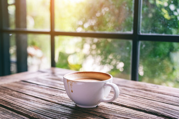 A white mug of hot coffee on wooden table in the morning