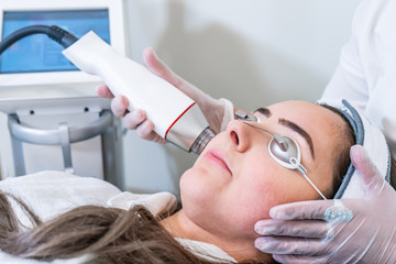 Beautician applying radio frequency microneedling handpiece to a woman's face for skin tightening treatments at a beauty clinic.