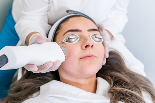 Beautician applying radio frequency microneedling handpiece to a woman's face for skin tightening treatments at a beauty clinic.