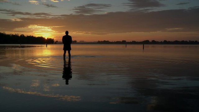 sunrise silhouette of a senior man standing in shallow water and  practicing a palm tree yoga pose, Boyd Lake State Park in northern Colorado