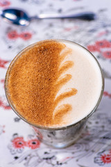 A wave pattern latte art on a glass of chai latte, with a defocused spoon in the background