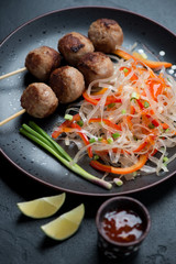 Nem nuong or fried vietnamese pork sausages on skewers with pho noodles, vertical shot, close-up