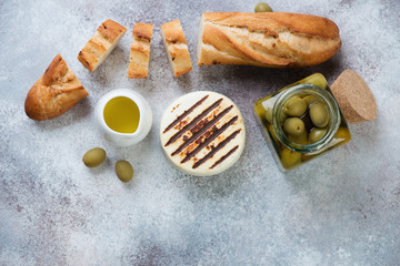 Grilled cheese, baguette and green olives over beige stone background with copyspace, flatlay, horizontal shot