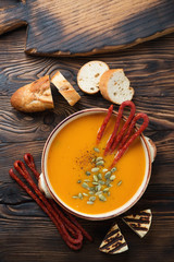 Pumpkin cream-soup with smoked meats, baguette and grilled cheese, top view on a rustic wooden background