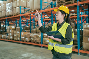 attractive woman in warehouse checking inventory levels of goods on shelf. lady worker in hard hat...