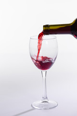 Red wine pouring from bottle into big glass on white background