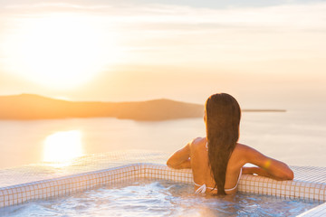 Luxury spa wellness resort woman relaxing in hot tub jacuzzi watching sunset over the Aegean sea in the Cyclades islands, Santorini, Greece, Europe. Hotel lifestyle.