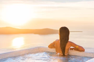 Fotobehang Luxury spa wellness resort woman relaxing in hot tub jacuzzi watching sunset over the Aegean sea in the Cyclades islands, Santorini, Greece, Europe. Hotel lifestyle. © Maridav