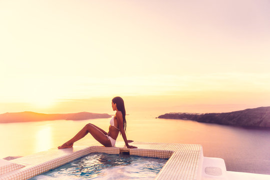 Luxury Resort Vacation Bikini Model Woman Relaxing Lying Down By Hot Tub Jacuzzi Private Swimming Pool Hotel Room Suite Balcony Sunset Over The Aegean Sea In The Cyclades Islands, Santorini, Greece.