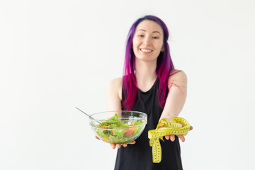 Slim young asian girl with colored hair is holds a measuring tape and holding a light vegetable salad in her hands posing on a white background. Healthy eating concept. Copyspace.