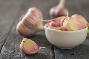 Garlic in a white bowl and on a black wooden table. Component of traditional medicine.