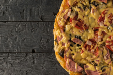 A piece of pizza on a black wooden table. The view from the top.