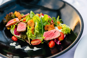 Close-up Medium Rare Tuna Salad (Green Coral, Red Coral, Tomato and Salmon Roe) with Touched Sea Urchin in black plate.