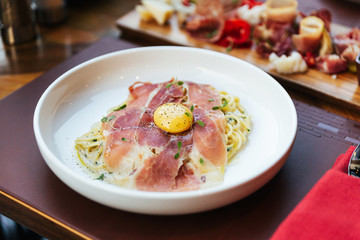 Fettuccine Carbonara with parma ham and yolk with black pepper. Served in white plate.