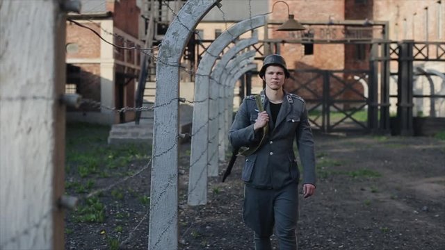A close view of a young male actor dressed as a German soldier near a barbed wire fence guarding a death camp