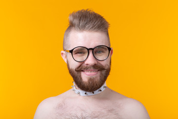 Young positive trendy man hipster with a mustache beard and fetish necklace in shirt posing on a yellow background. Concept of rock and subculture. - obrazy, fototapety, plakaty