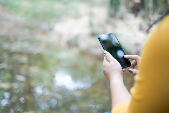 woman's hand holding and using smartphone, black screen with blur nature background. subject is blur.