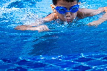 close up asian boy ware a blue glasses diving and swimming in pool and blue refreshing water.