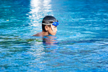 Portrait of asian boy diving and swimming in pool and blue refreshing water.