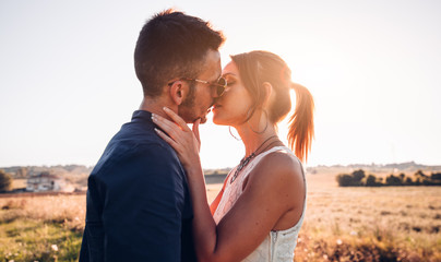 Romantic couple kissing outdoor at sunset on a field.