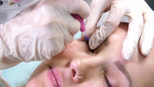 Microblading eyebrows in a beauty salon. Semi-permanent makeup. Professional stylist lengthening female lashes. Eyelash extension procedure - master and a client in a beauty salon