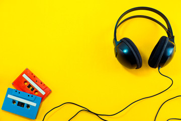Top view of Headphone and blue classic tape cassette against yellow isolated background. Listening music theme.