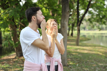 young caucasian couple people who wearing sport suit are in love. yawning while exercise in park on summer time with nature green trees