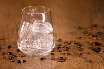 Detail of roasted coffee seeds on the table around a glass cup with ice cubes