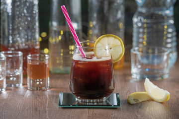 A tasty cocktail with lemon slices accompanied by shot's and tequila bottles on a wooden table