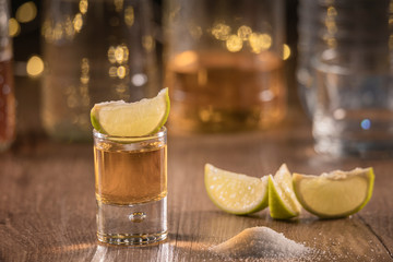 Lime slices on the table and a tasty shot's of tequila with tequila bottles on the bottom and salt...