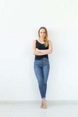 Style and people concept - young woman in jeans standing over the white wall and looks like sexy