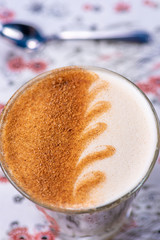 A wave pattern latte art on a glass of chai latte, with a defocused spoon in the background