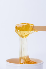 Liquid yellow sugar paste or wax for depilation on a stick close-up on a white background