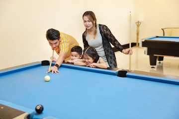 group of happiness asian family father, mother, son and daughter playing billiard or snooker on...