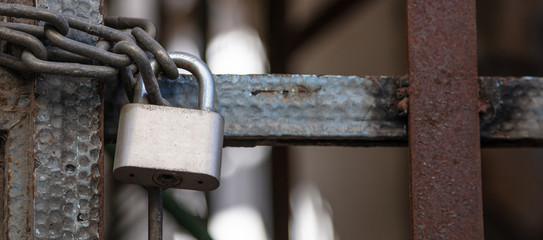 Heavy metal padlock with chain closeup on an entrance gate.