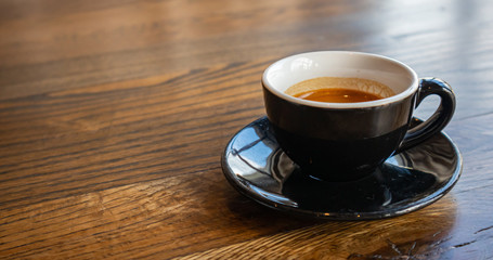 Espresso cup, black color with saucer on wooden table