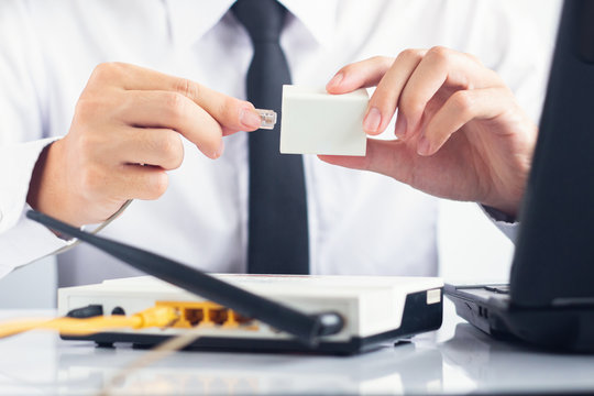 Male IT support holding RJ11 cable connecting ADSL Splitter with modem and laptop on white table