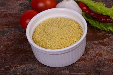 Raw couscous in the bowl served salad leaves, tomato and pepper