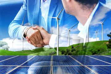 Double exposure graphic of business people handshake over wind turbine farm and green renewable...