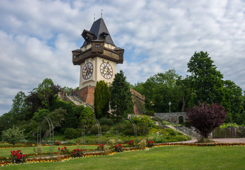 Fototapeta na wymiar The famous clock tower (Grazer Uhrturm) and gardens on Shlossberg hill, with a cloudy sky, in Graz, Styria region, Austria